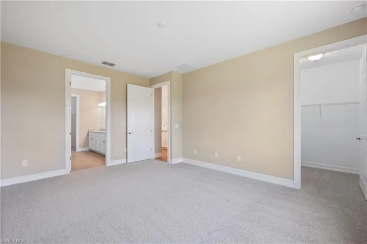 Unfurnished bedroom featuring a spacious closet, a closet, connected bathroom, and light colored carpet