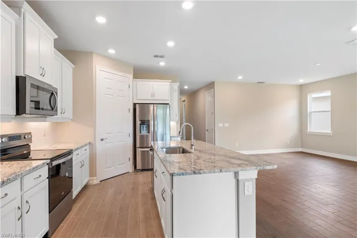 Kitchen featuring stainless steel appliances, sink, a kitchen island with sink, light wood-type flooring, and white cabinetry