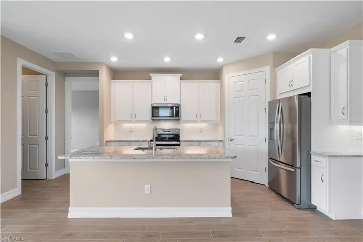 Kitchen featuring decorative backsplash, appliances with stainless steel finishes, a kitchen island with sink, and white cabinetry