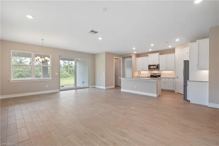 Kitchen featuring a notable chandelier, white cabinets, sink, a center island with sink, and appliances with stainless steel finishes