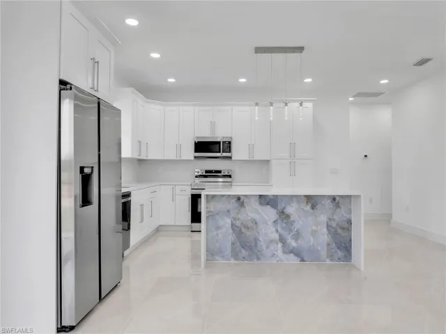 Kitchen with stainless steel appliances, recessed lighting, pendant lighting, white cabinets, and light stone countertops