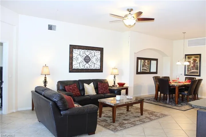 Living room with light tile patterned flooring, arched walkways, ceiling fan, and visible vents