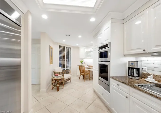Kitchen with appliances with stainless steel finishes, dark stone counters, decorative backsplash, white cabinets, and ornamental molding