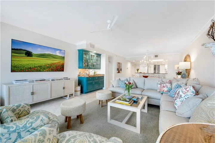 Living room featuring crown molding, light tile patterned floors, and ceiling fan with notable chandelier