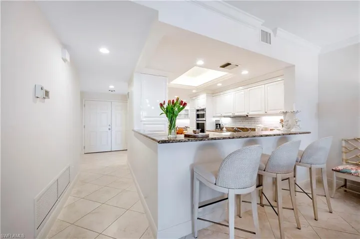 Kitchen featuring kitchen peninsula, tasteful backsplash, ornamental molding, dark stone counters, and white cabinets