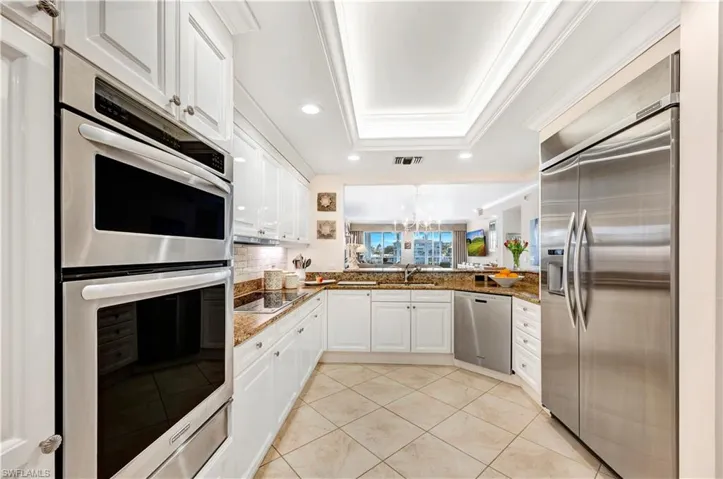 Kitchen featuring kitchen peninsula, appliances with stainless steel finishes, dark stone counters, a tray ceiling, and white cabinetry