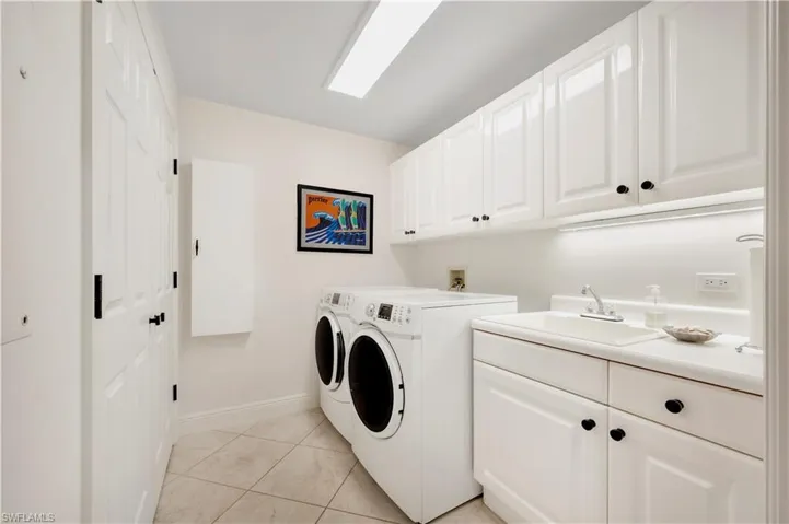 Laundry room featuring washer and dryer, light tile patterned flooring, cabinets, and sink