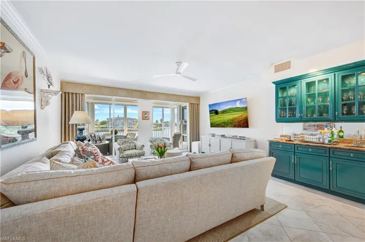 Tiled living room with ceiling fan, wet bar, and crown molding