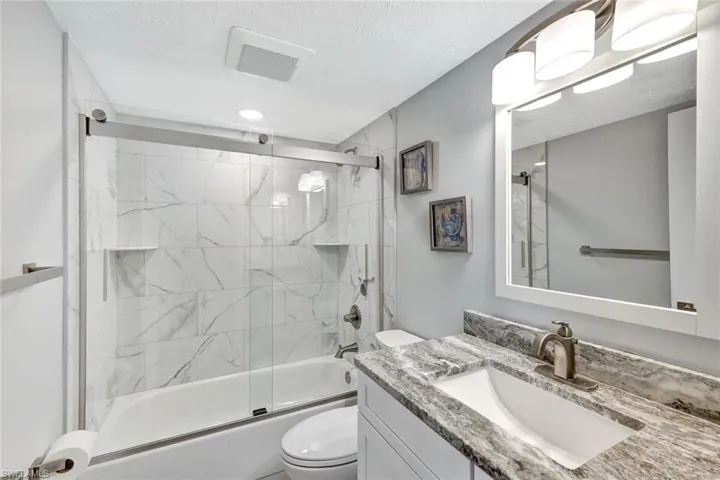 Full bathroom featuring shower / bath combination with glass door, a textured ceiling, vanity, and toilet