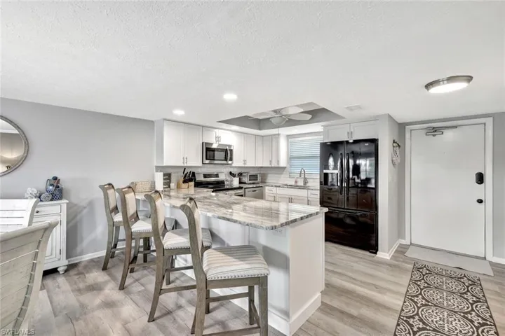 Kitchen with kitchen peninsula, appliances with stainless steel finishes, white cabinetry, and light stone countertops