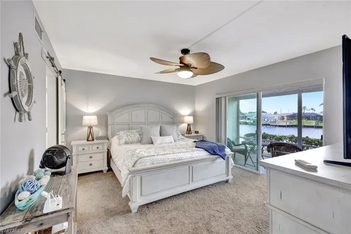Carpeted bedroom with a barn door, ceiling fan, a water view, and access to exterior