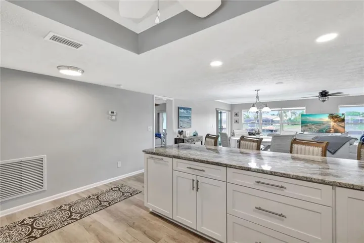 Kitchen featuring ceiling fan with notable chandelier, light hardwood / wood-style flooring, white cabinetry, and light stone counters