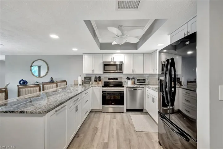 Kitchen with kitchen peninsula, white cabinetry, stainless steel appliances, and light wood-type flooring