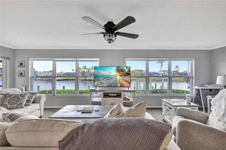 Carpeted living room featuring ceiling fan and ornamental molding