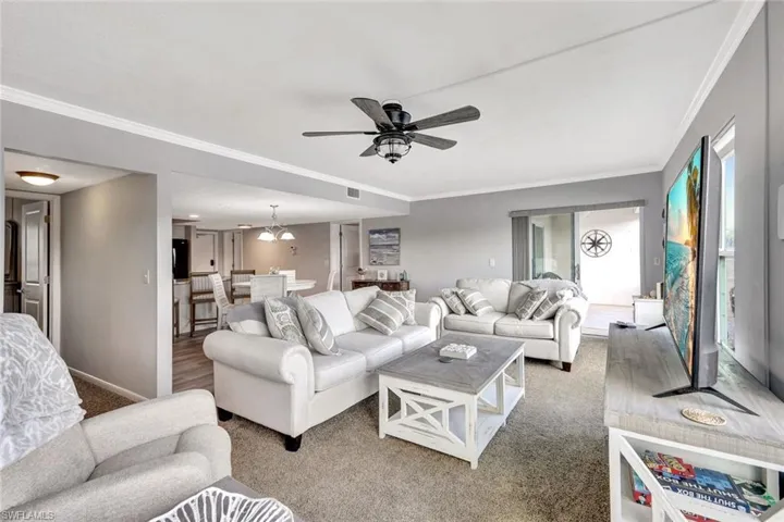 Living room featuring carpet flooring, crown molding, and ceiling fan with notable chandelier