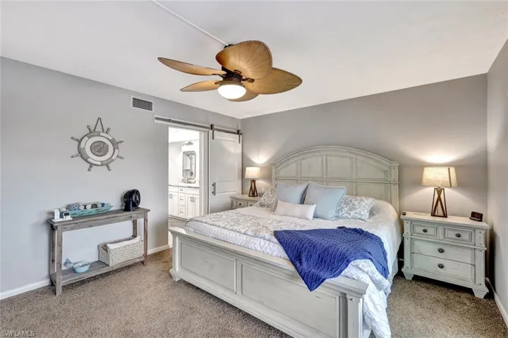 Bedroom featuring connected bathroom, a barn door, ceiling fan, and light carpet