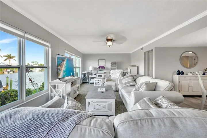 Living room featuring ceiling fan, a water view, carpet floors, and crown molding