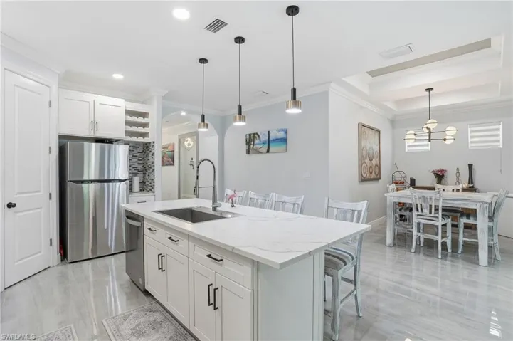 Kitchen featuring white cabinets, ornamental molding, stainless steel appliances, a kitchen breakfast bar, and light stone counters