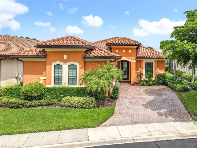 Stucco exterior featuring a terracotta tile roof, arched windows, and a paver driveway