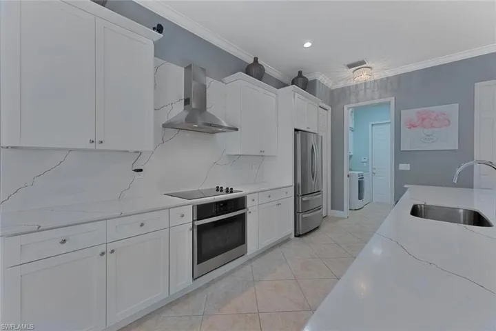 Kitchen with wall chimney range hood, ornamental molding, washer / dryer, stainless steel appliances, and a sink