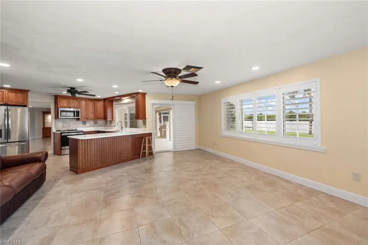Kitchen with open floor plan, appliances with stainless steel finishes, ceiling fan, light countertops, and brown cabinets
