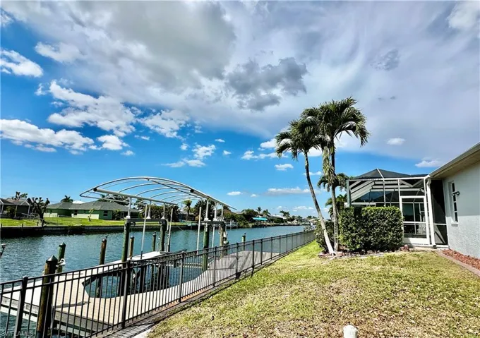 View of the Captain's walk covered boat lift at the retaining wall along the fencing that surrounds the property.  Note the entry screendoor from this side of the pool cage.  The adjacent window is the Second Primary Ensuite.