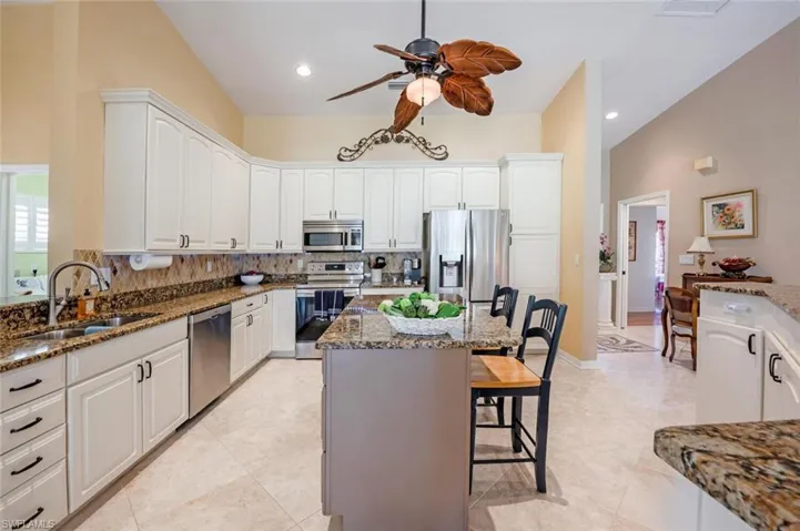 Kitchen with a sink, dark stone counters, a kitchen bar, ceiling fan, and appliances with stainless steel finishes