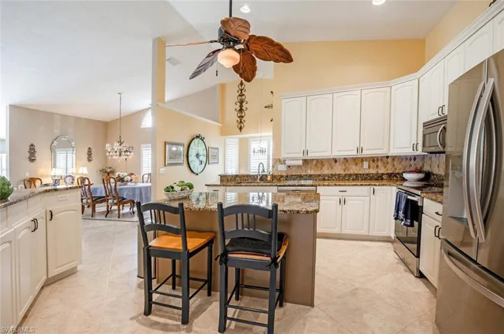 Kitchen featuring a kitchen breakfast bar, a sink, ceiling fan with notable chandelier, stone countertops, and stainless steel appliances