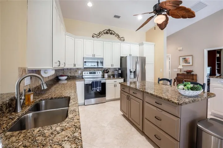 Kitchen with stainless steel appliances, backsplash, a ceiling fan, a sink, and a kitchen island