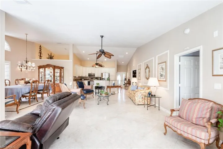 Living room with ceiling fan with notable chandelier, baseboards, high vaulted ceiling, and light tile patterned floors