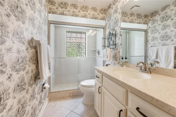 Bathroom featuring wallpapered walls, tile patterned flooring, visible vents, toilet, and a stall shower
