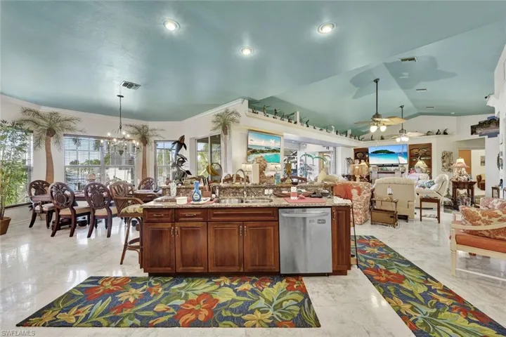 Kitchen with light stone countertops, stainless steel dishwasher, a kitchen bar, light marble finish floors, and vaulted ceiling