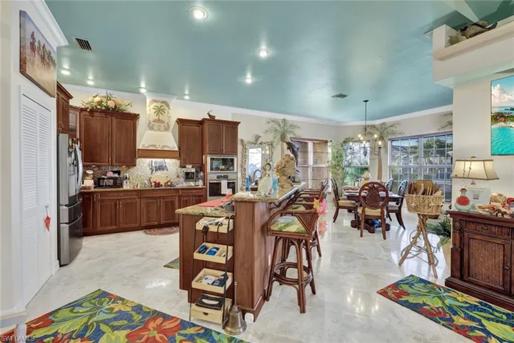 Kitchen featuring a breakfast bar area, hanging light fixtures, appliances with stainless steel finishes, crown molding, and light stone counters