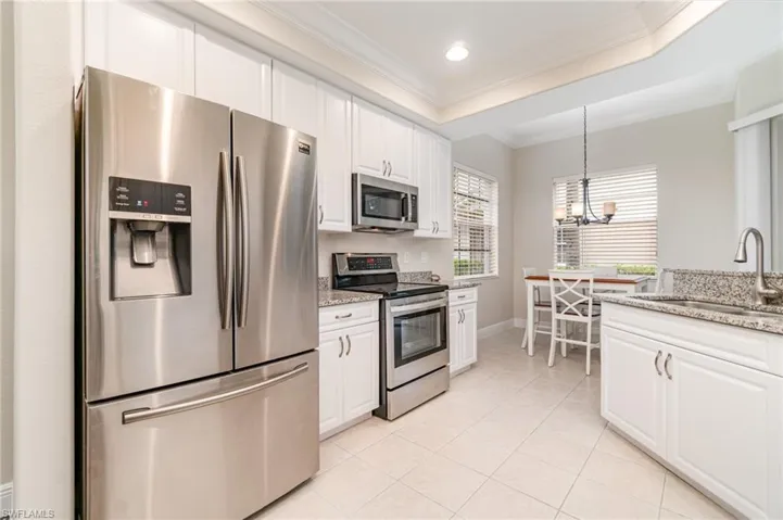 Kitchen featuring light stone counters, ornamental molding, white cabinets, dishwasher, and hanging light fixtures