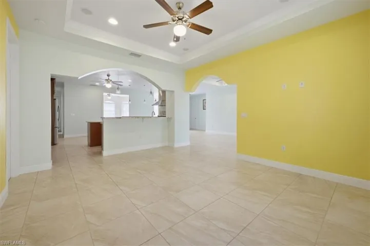 Spacious interior featuring large format tile flooring, crown molding, a tray ceiling with recessed lighting and a ceiling fan, and arched doorways