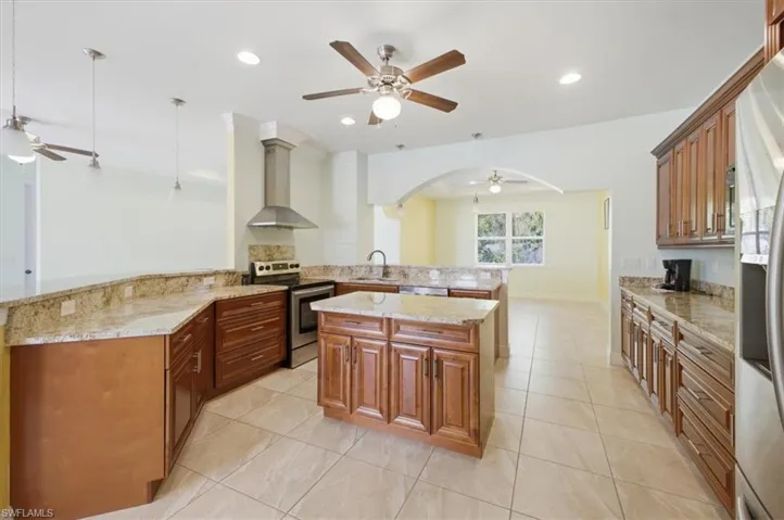 Spacious kitchen featuring warm wood cabinetry, light granite countertops, a central island, stainless steel appliances, and tile flooring