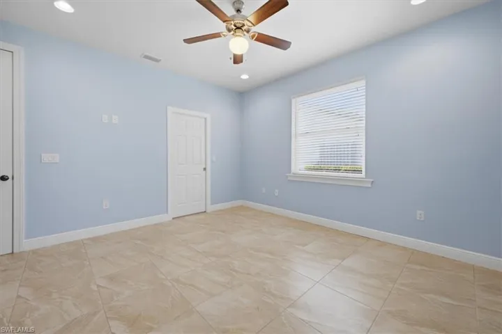Spacious room featuring neutral tile flooring, light blue walls, and a ceiling fan with integrated lighting