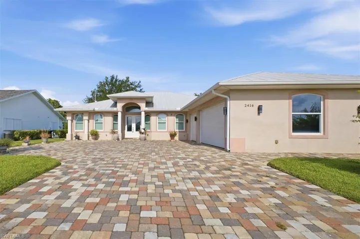 Contemporary stucco exterior featuring an arched entryway with double doors, symmetrical columns, and an integrated two-car garage