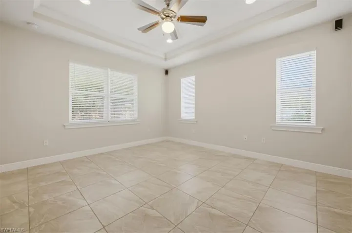 Spacious interior room featuring light-toned tile flooring, tray ceiling with recessed lighting, and a ceiling fan