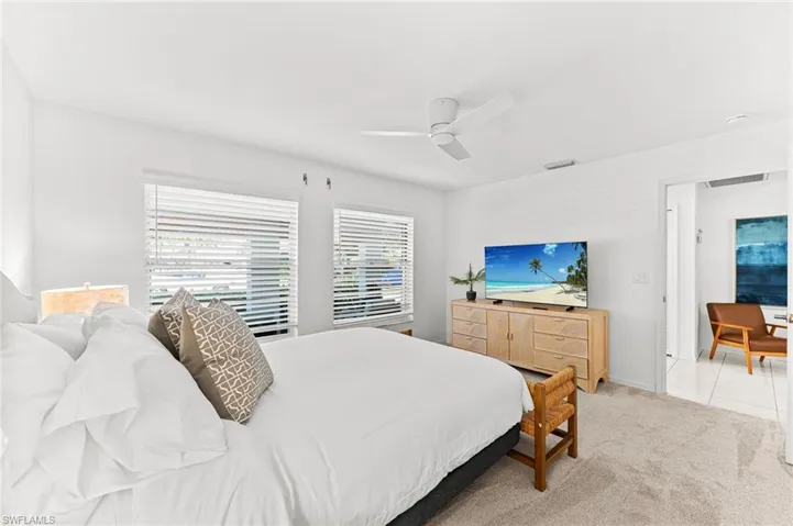 Bedroom with light colored carpet, ceiling fan, and light tile patterned flooring