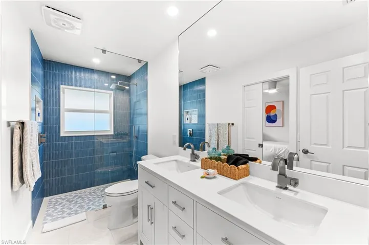 Ensuite bathroom with double vanity, a walk in shower, light tile patterned floors, and recessed lighting