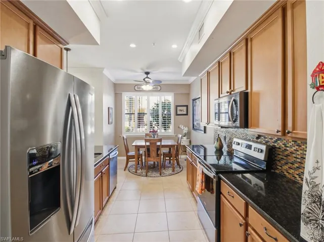 Kitchen featuring stainless steel appliances, dark stone countertops, ornamental molding, light tile patterned floors, and a ceiling fan