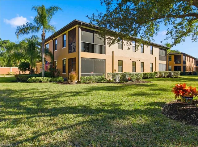 Rear view of property featuring a lawn, stucco siding, a sunroom, and a balcony