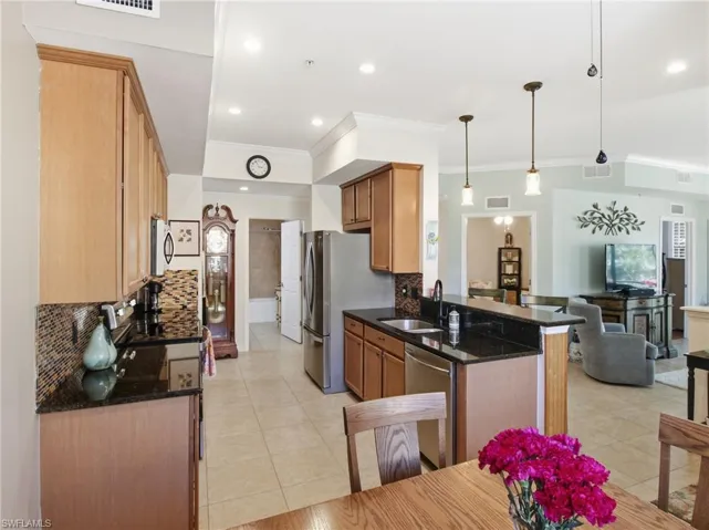 Kitchen with tasteful backsplash, stainless steel appliances, hanging light fixtures, dark stone counters, and ornamental molding