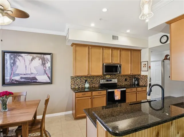Kitchen with stainless steel appliances, dark stone counters, decorative backsplash, ornamental molding, and a peninsula