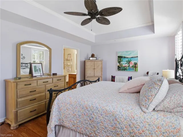 Bedroom with ornamental molding, dark wood-style flooring, ensuite bath, ceiling fan, and a raised ceiling