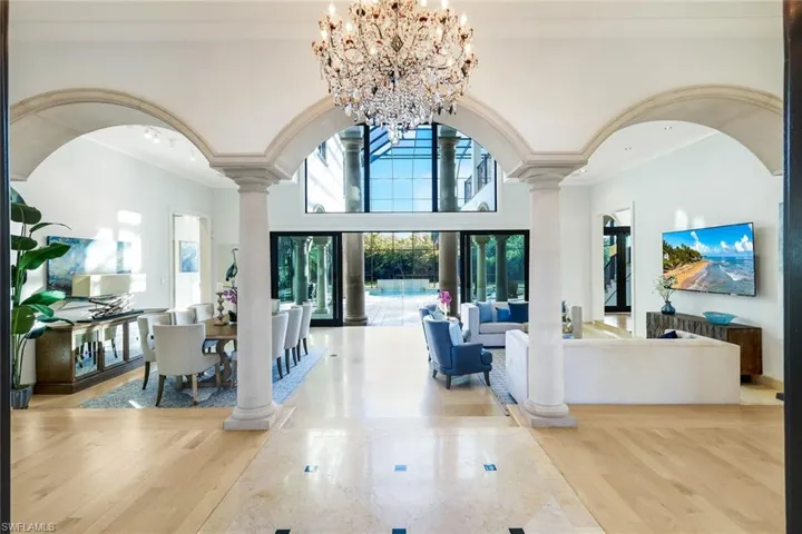 Living area with ornate columns, a chandelier, light wood flooring, crown molding, and a high ceiling