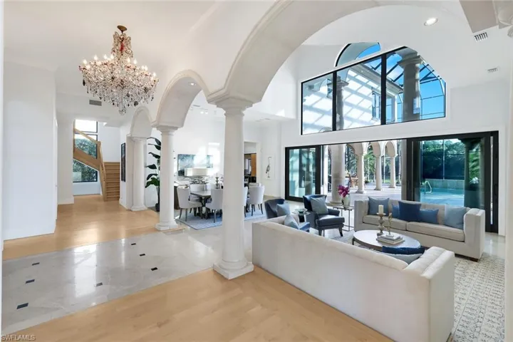 Living room with decorative columns, a chandelier, a towering ceiling, and stairway
