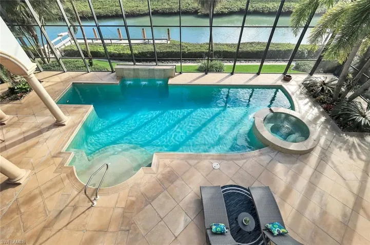 View of pool featuring a pool with connected hot tub, glass enclosure, and a water view