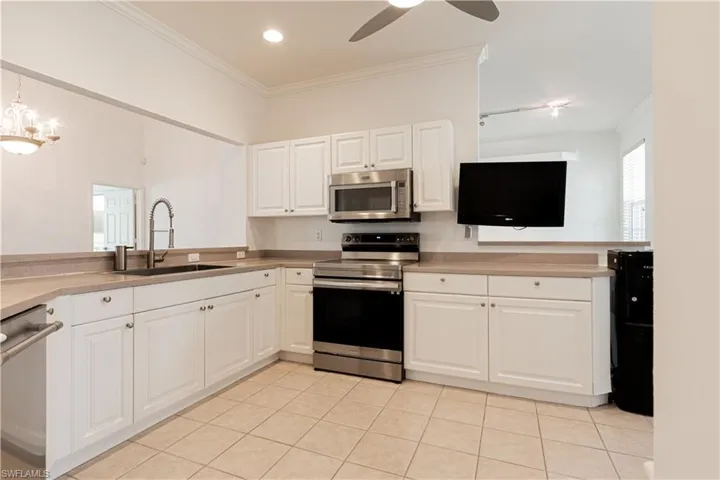 Recently painted white -Kitchen featuring light tile patterned flooring, white cabinets, crown molding, sink, and appliances with stainless steel finishes